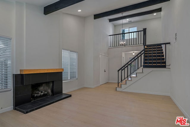 living room with hardwood / wood-style floors, beam ceiling, a high ceiling, a tiled fireplace, and a chandelier