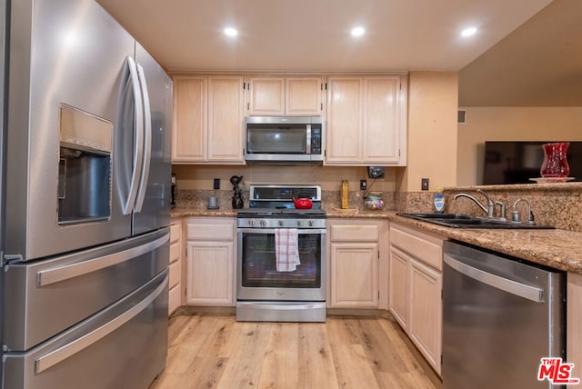 kitchen with sink, light wood-type flooring, kitchen peninsula, stainless steel appliances, and light stone countertops