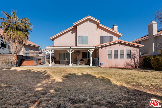 rear view of property featuring a lawn, a hot tub, and a patio