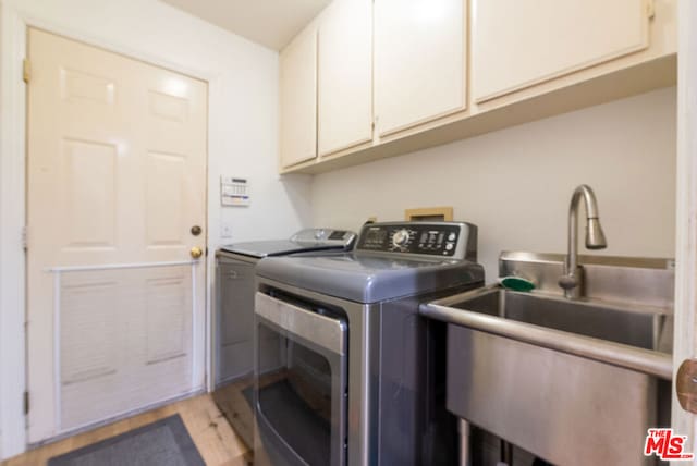 laundry room with light hardwood / wood-style flooring, sink, washer and clothes dryer, and cabinets