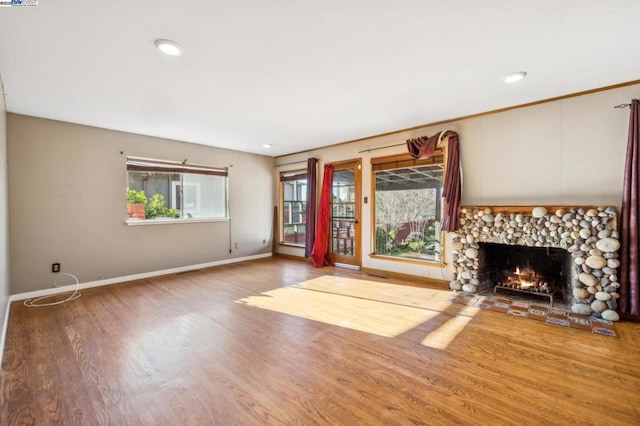 unfurnished living room with hardwood / wood-style flooring and a stone fireplace