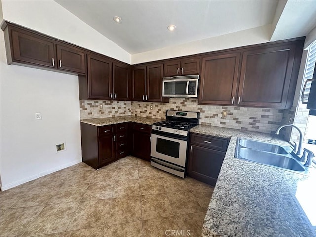 kitchen featuring lofted ceiling, appliances with stainless steel finishes, light stone countertops, and sink