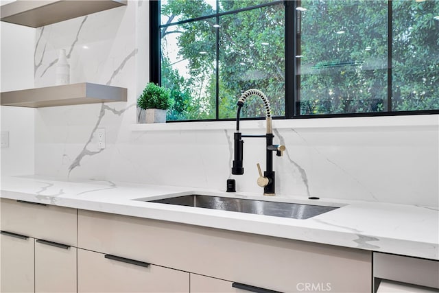 details featuring light stone counters, sink, white cabinetry, and tasteful backsplash