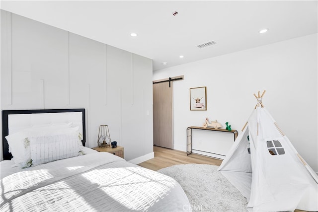 bedroom with a barn door and light hardwood / wood-style floors