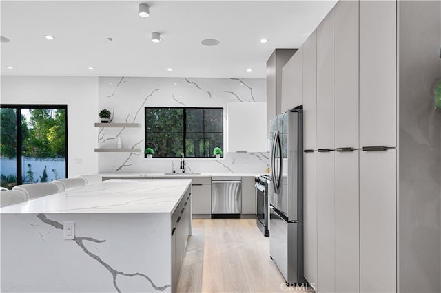 kitchen with sink, decorative backsplash, light stone counters, light hardwood / wood-style floors, and stainless steel appliances