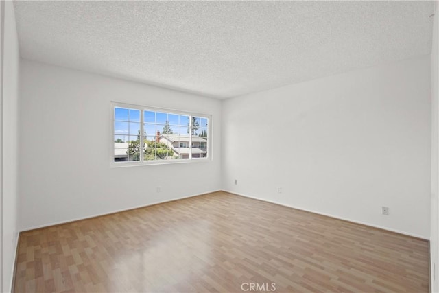 empty room with baseboards, a textured ceiling, and wood finished floors