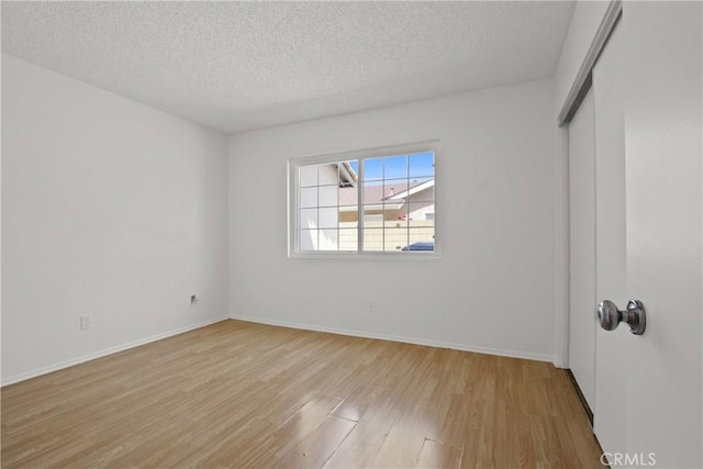 unfurnished bedroom with a textured ceiling, baseboards, light wood finished floors, and a closet