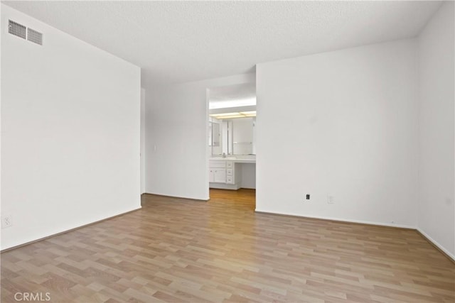 unfurnished room featuring a textured ceiling, visible vents, and light wood-style floors
