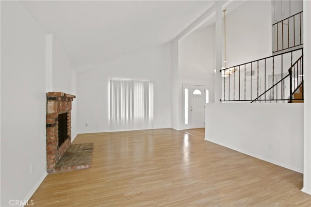 unfurnished living room with a brick fireplace, wood finished floors, high vaulted ceiling, baseboards, and stairs