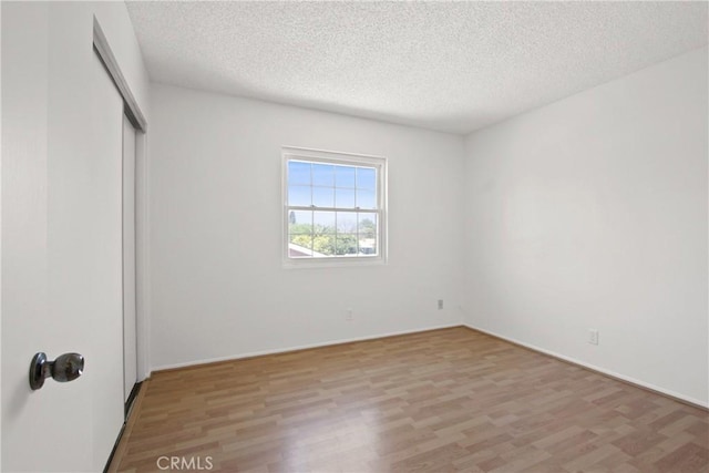 unfurnished bedroom featuring a textured ceiling, a closet, and light wood-style flooring