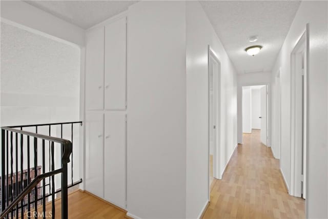 corridor featuring baseboards, a textured ceiling, an upstairs landing, and light wood-style flooring