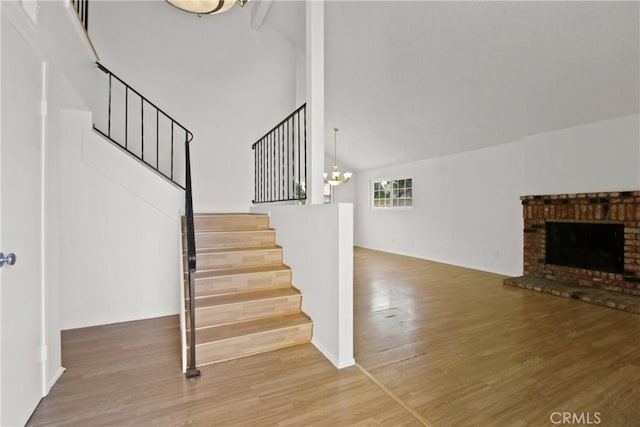 stairway with a brick fireplace, high vaulted ceiling, a chandelier, baseboards, and wood finished floors