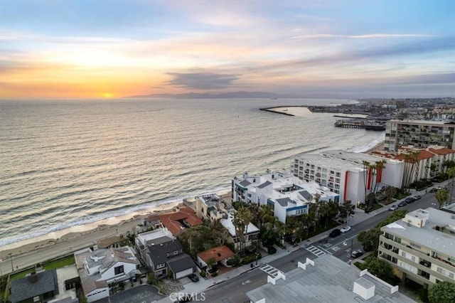 aerial view at dusk featuring a water view and a view of the beach