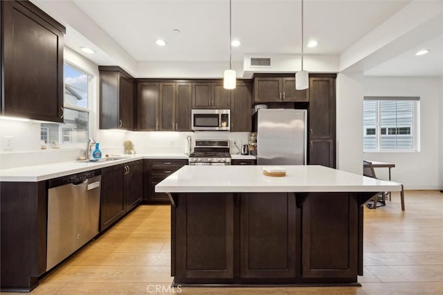 kitchen with stainless steel appliances, a kitchen island, hanging light fixtures, and sink