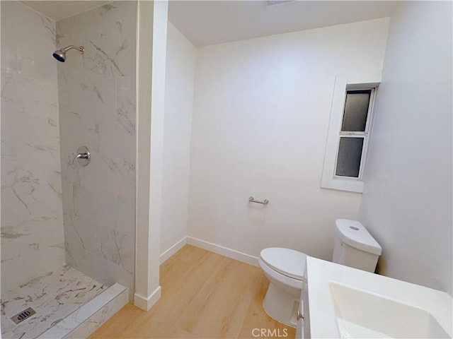 bathroom featuring hardwood / wood-style flooring, vanity, tiled shower, and toilet