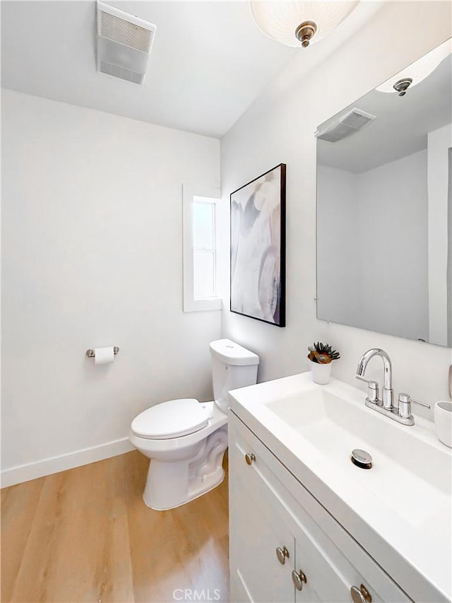 half bathroom with visible vents, toilet, vanity, and wood finished floors
