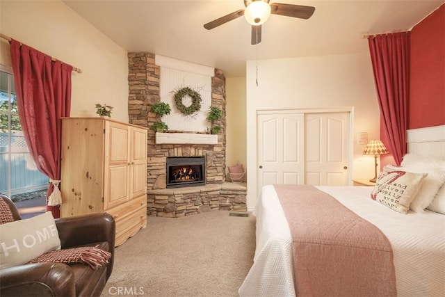 carpeted bedroom with a stone fireplace, a closet, and ceiling fan