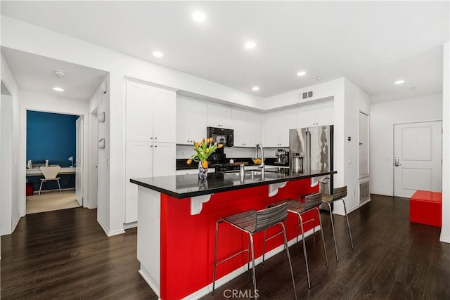 kitchen featuring a breakfast bar area, dark hardwood / wood-style floors, a center island with sink, and white cabinets