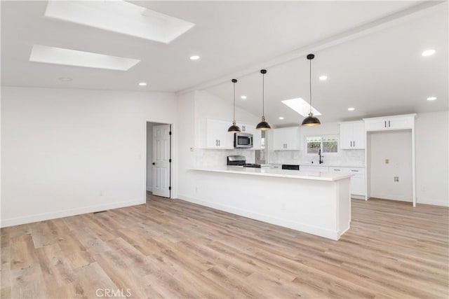 kitchen with decorative light fixtures, lofted ceiling with skylight, white cabinets, and range