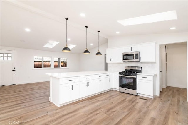 kitchen with appliances with stainless steel finishes, white cabinetry, hanging light fixtures, vaulted ceiling with skylight, and kitchen peninsula