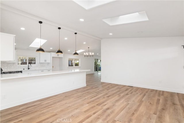 kitchen featuring sink, white cabinetry, pendant lighting, vaulted ceiling with skylight, and backsplash