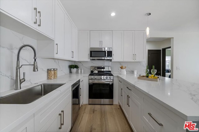 kitchen with sink, appliances with stainless steel finishes, hanging light fixtures, white cabinets, and light wood-type flooring