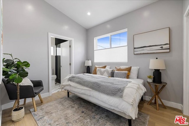 bedroom with lofted ceiling, connected bathroom, and light hardwood / wood-style flooring