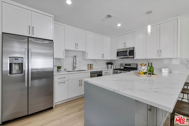 kitchen featuring sink, a breakfast bar area, white cabinetry, pendant lighting, and stainless steel appliances