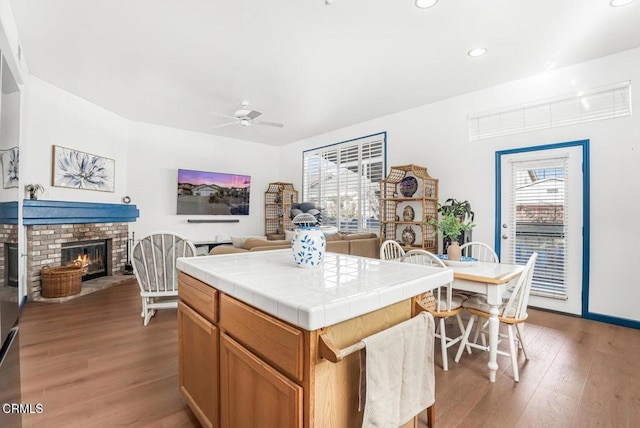 kitchen with ceiling fan, hardwood / wood-style floors, a center island, a fireplace, and tile countertops