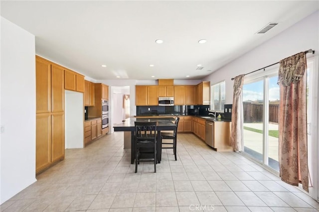 kitchen featuring sink, light tile patterned floors, appliances with stainless steel finishes, a kitchen breakfast bar, and a kitchen island