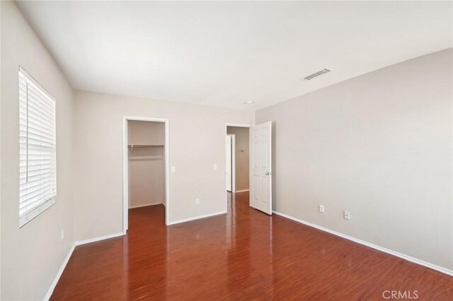 unfurnished bedroom with dark hardwood / wood-style flooring, a walk in closet, and a closet