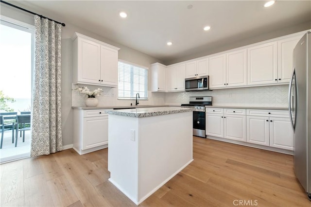 kitchen with a kitchen island, appliances with stainless steel finishes, tasteful backsplash, white cabinets, and light wood-type flooring