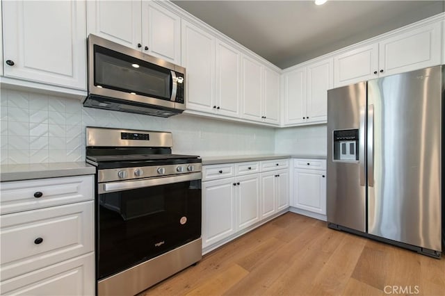 kitchen featuring stainless steel appliances, decorative backsplash, white cabinets, and light hardwood / wood-style flooring