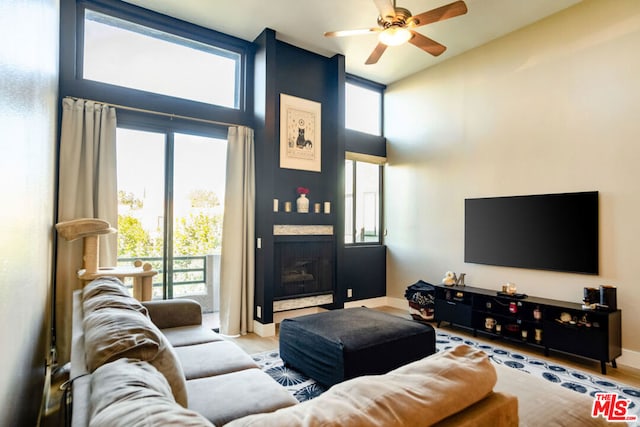 living room with a fireplace, light hardwood / wood-style floors, ceiling fan, and a high ceiling