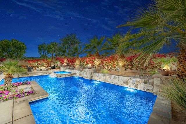 pool at night featuring an in ground hot tub, pool water feature, and a patio area