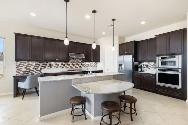 kitchen featuring appliances with stainless steel finishes, pendant lighting, sink, a kitchen bar, and a center island with sink