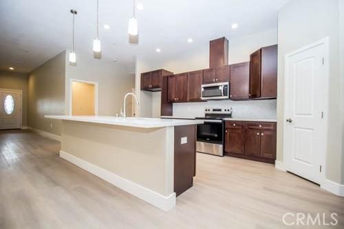 kitchen featuring appliances with stainless steel finishes, decorative light fixtures, light hardwood / wood-style floors, and an island with sink