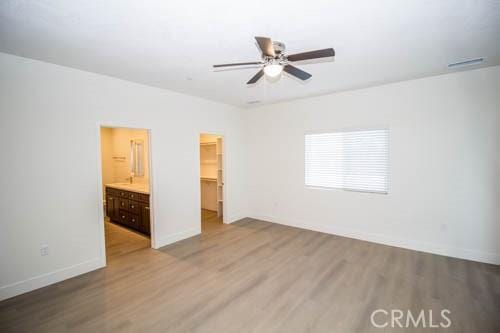 unfurnished bedroom featuring ensuite bathroom, a spacious closet, hardwood / wood-style floors, and a closet