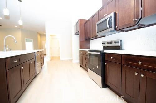 kitchen featuring stainless steel appliances, dark brown cabinets, sink, and pendant lighting