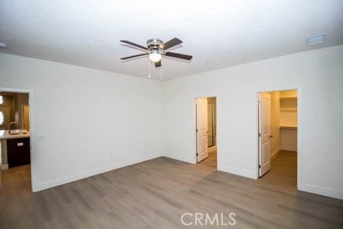 unfurnished bedroom featuring sink, ceiling fan, hardwood / wood-style floors, a walk in closet, and a closet