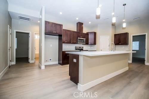 kitchen featuring pendant lighting, dark brown cabinetry, an island with sink, and appliances with stainless steel finishes