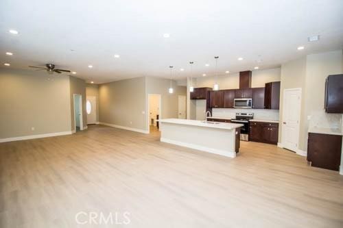 kitchen with sink, light hardwood / wood-style flooring, appliances with stainless steel finishes, hanging light fixtures, and a center island with sink