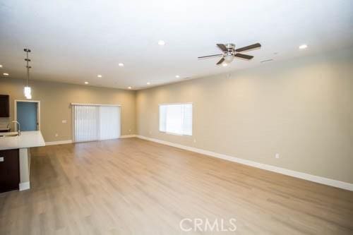 unfurnished living room featuring sink, light hardwood / wood-style floors, and ceiling fan