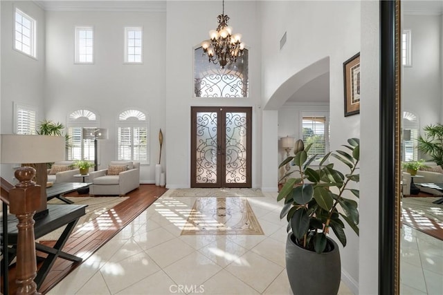 foyer entrance with light tile patterned floors, crown molding, a notable chandelier, and french doors