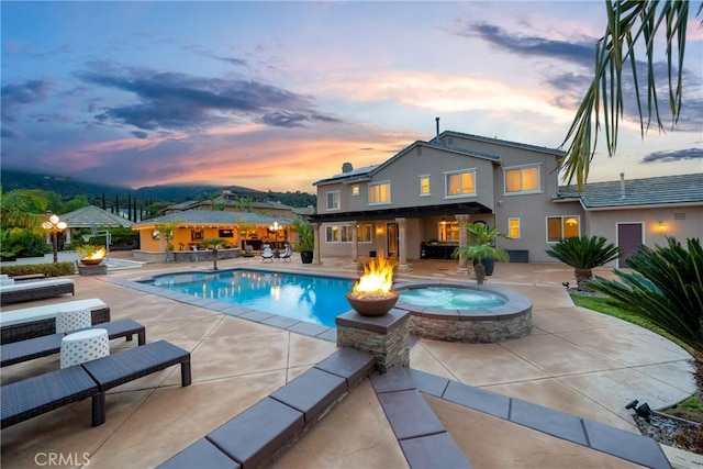 pool at dusk featuring a fire pit, a gazebo, a patio area, and an in ground hot tub