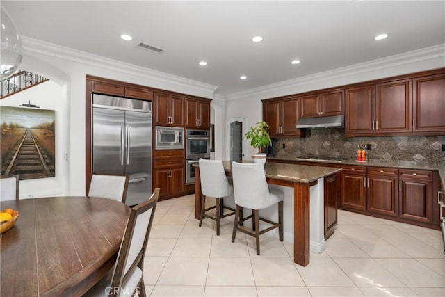 kitchen featuring built in appliances, light tile patterned floors, dark stone counters, and a kitchen island