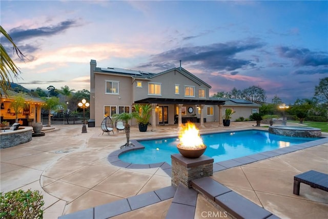 pool at dusk with a fire pit, a patio area, and an in ground hot tub