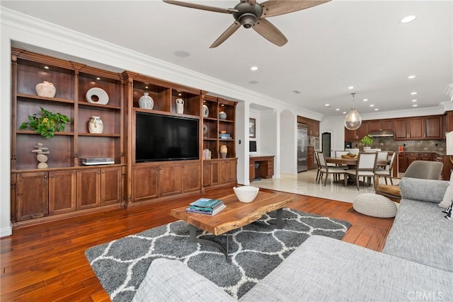 living room featuring dark wood-type flooring, ceiling fan, and ornamental molding