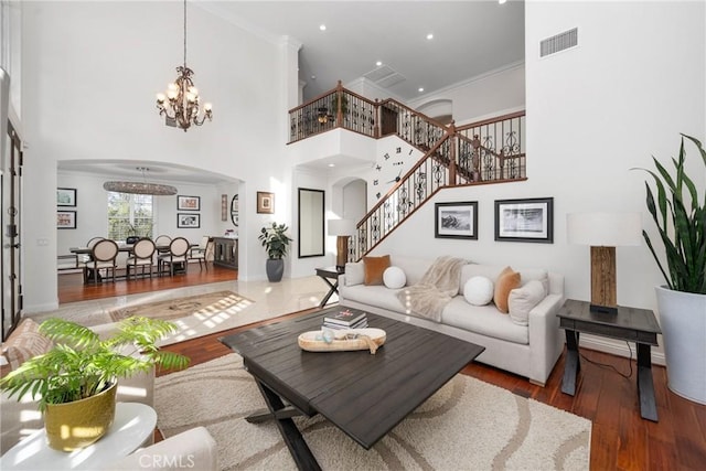 living room featuring hardwood / wood-style floors, crown molding, a chandelier, and a high ceiling