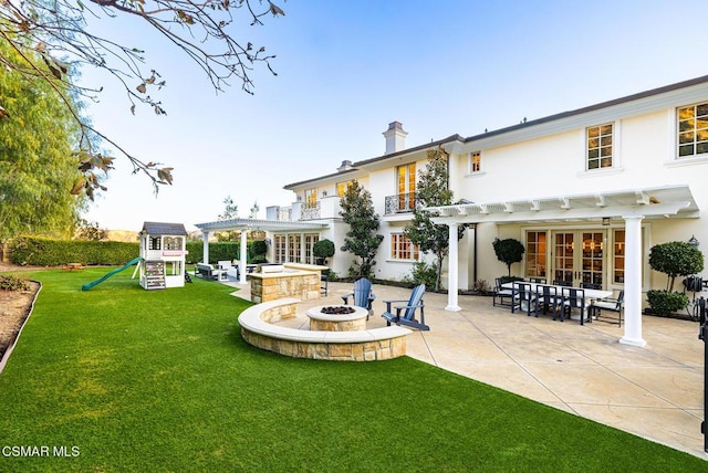 back of house featuring a yard, a pergola, a playground, a fire pit, and a patio